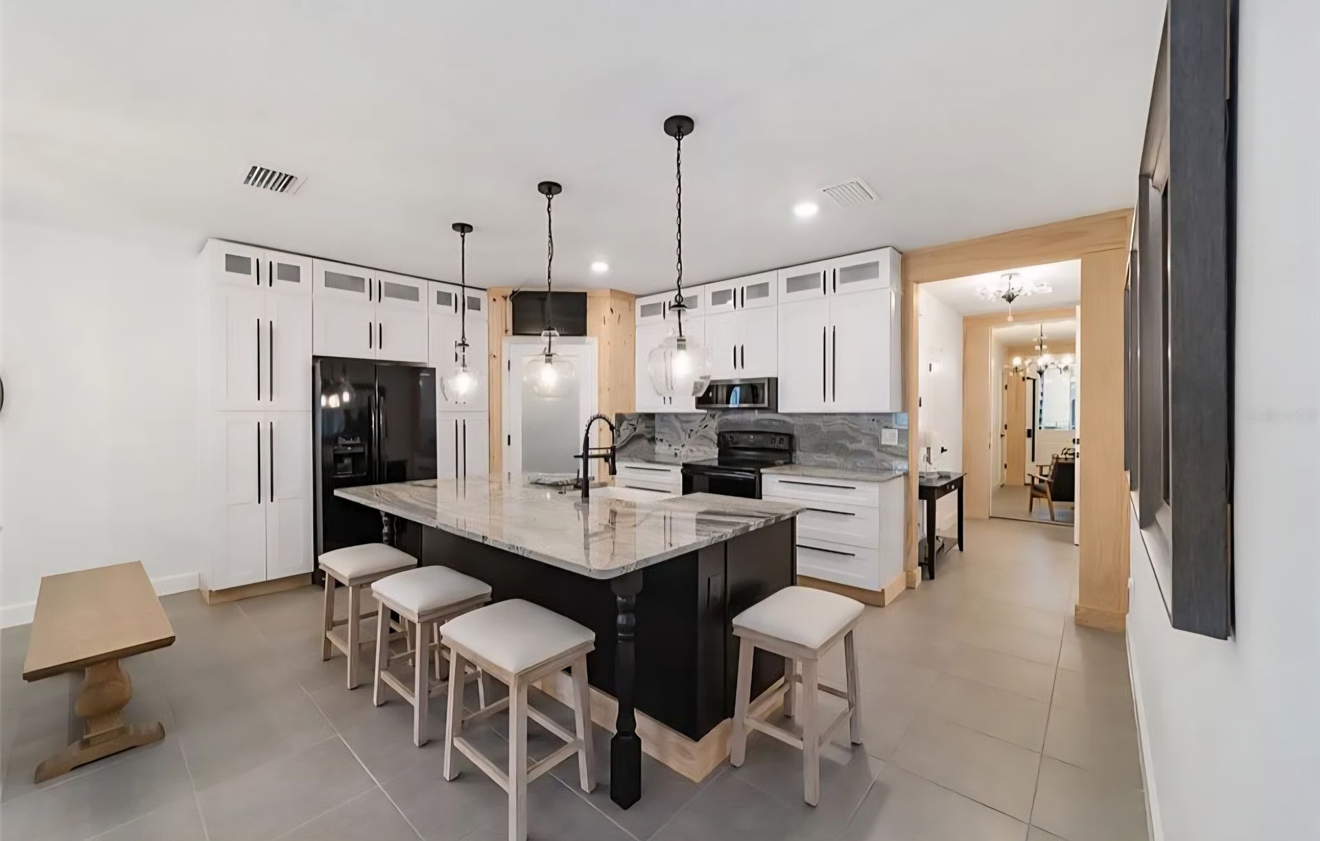 Modern white kitchen with black island, pendant lights, bar stools, and tiled floor