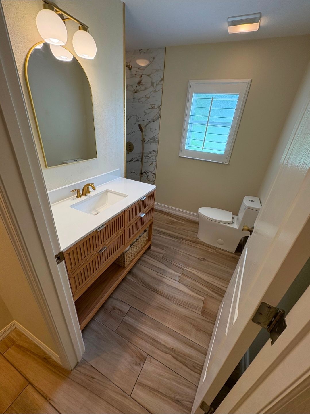Bright bathroom with white vanity, wood cabinet, mirror, and window with blinds.