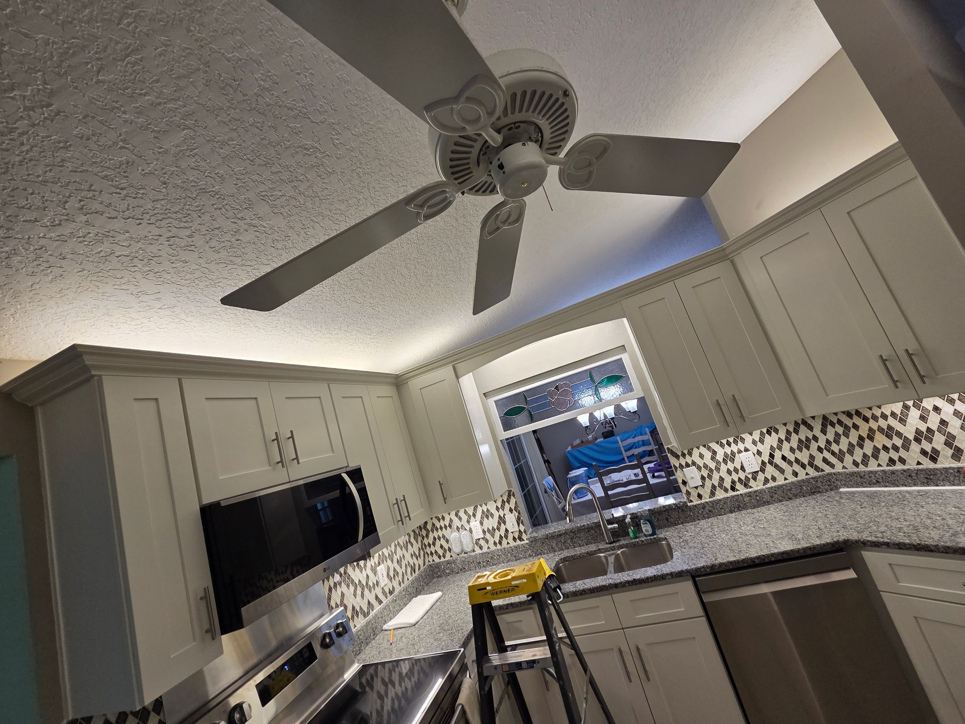 Modern kitchen with gray cabinets, ceiling fan, mosaic backsplash, and a window over the sink