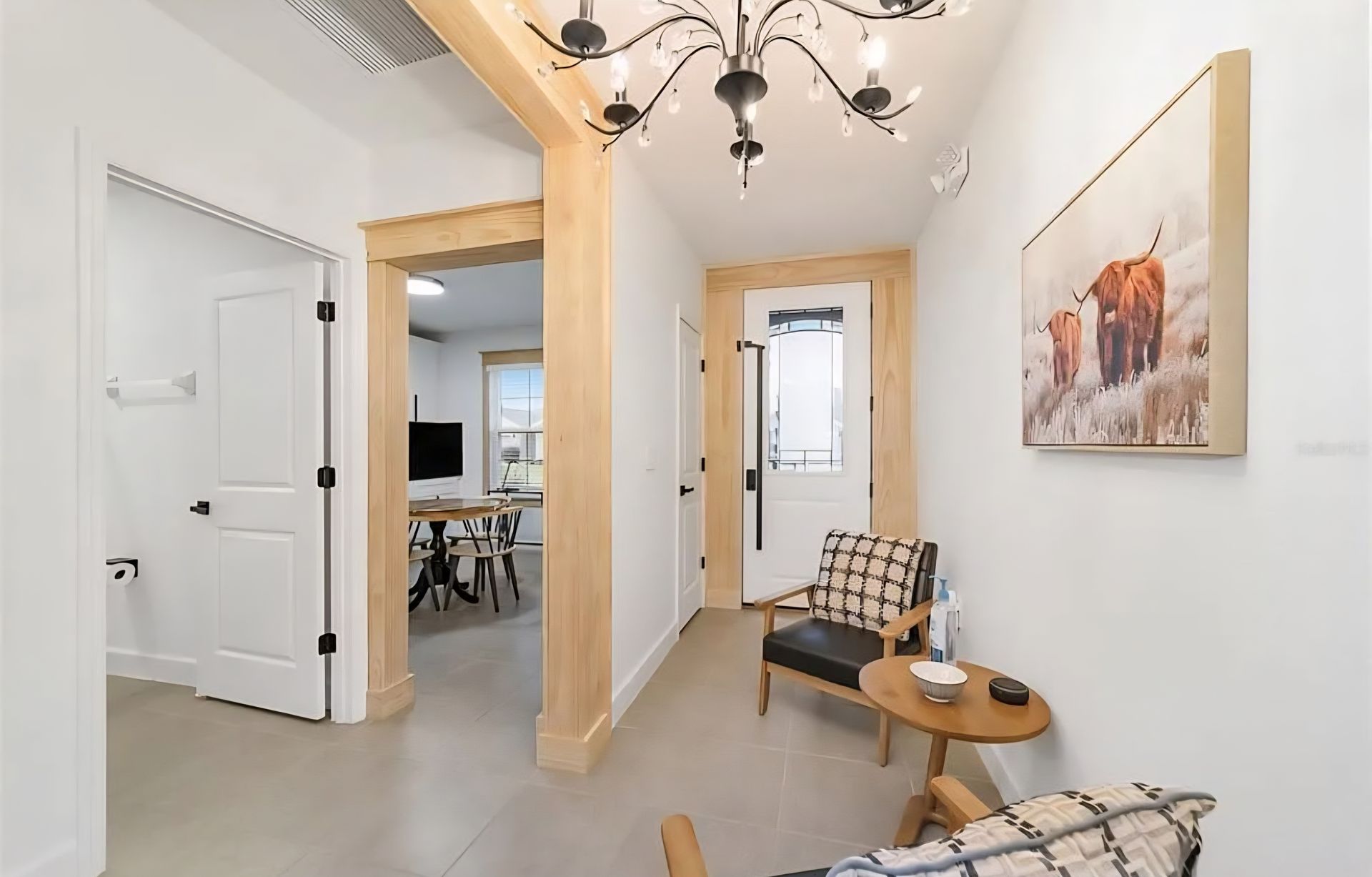 Bright hallway with wood beams, chandelier, white walls, a bench, and doorway to a dining area