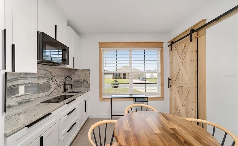 Bright kitchen with white cabinets, marble countertop, wood table, and barn-door pantry by a window.