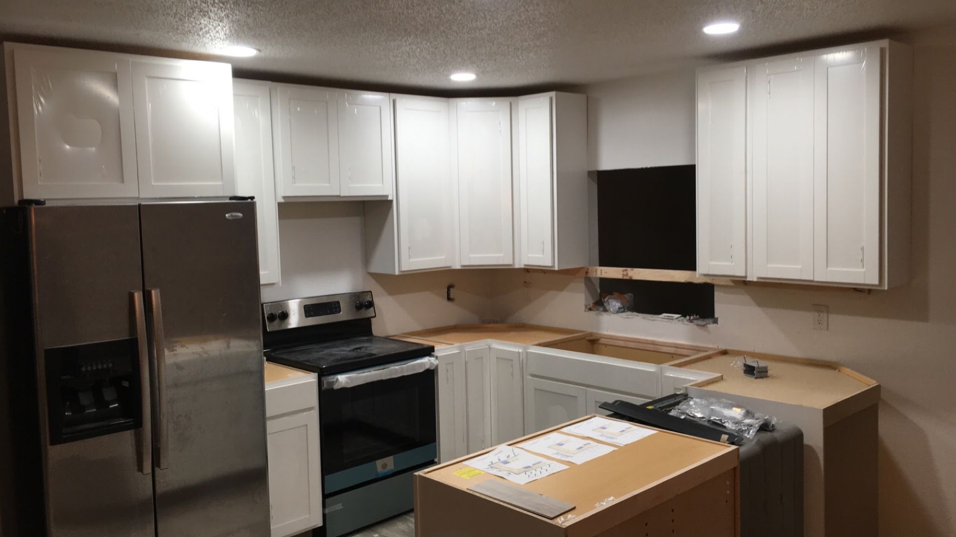 Modern kitchen with white cabinets, stainless steel fridge, stove, and a central island under recessed lights