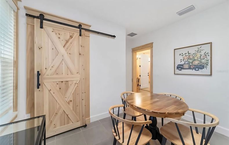 Rustic sliding barn door beside a round wooden table with chairs in a bright room