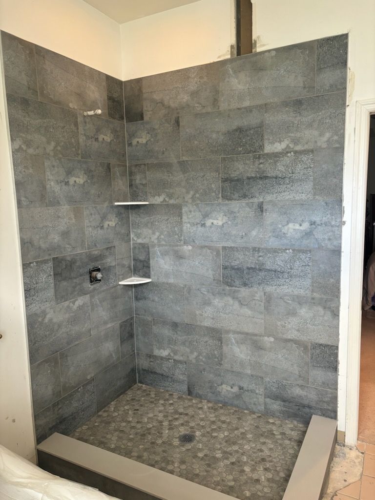 Modern tiled walk-in shower with gray stone walls, pebble floor, and built-in corner shelves