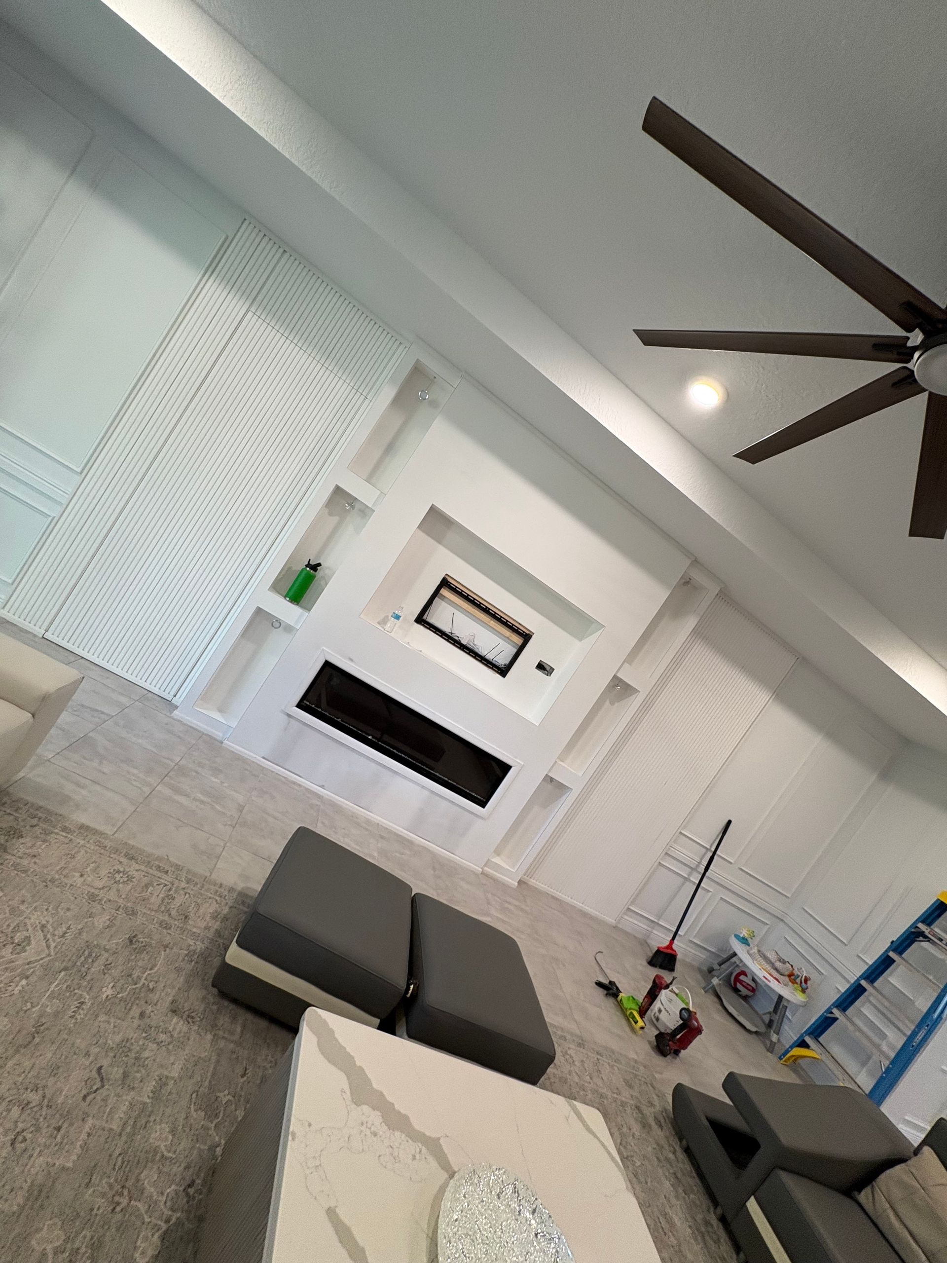 Tilted view of a modern living room with gray sofas, fireplace, blinds, and a ceiling fan