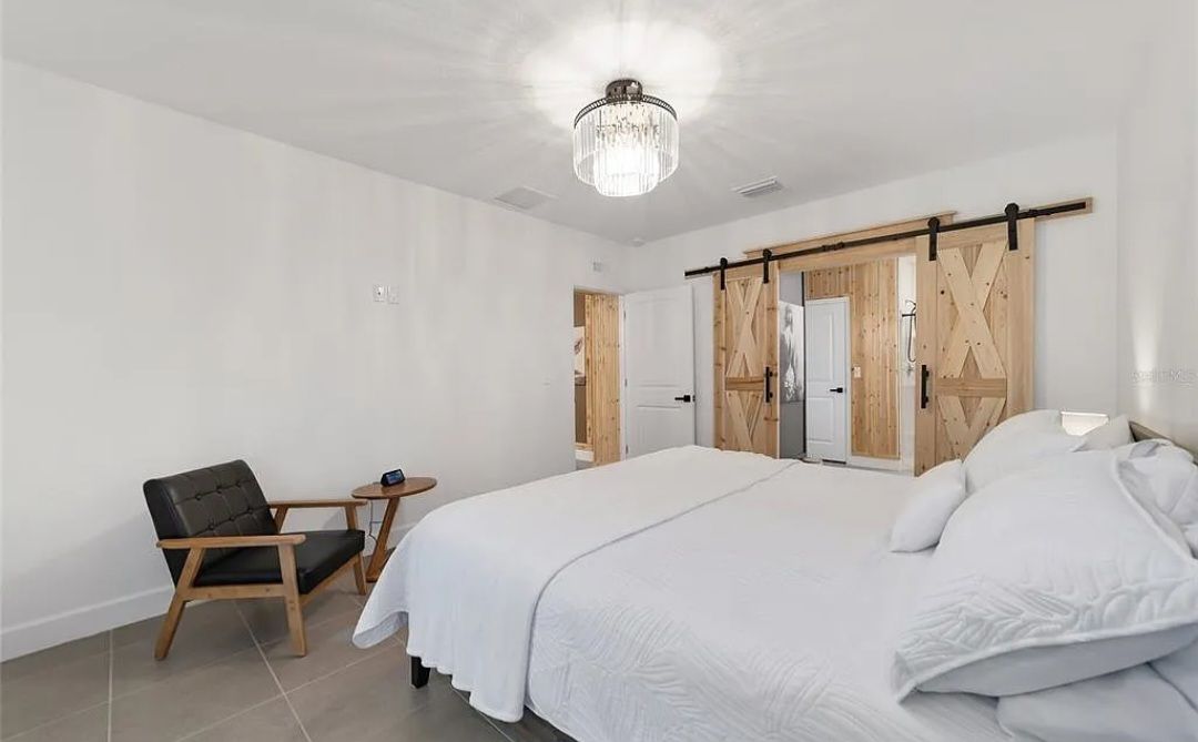 Bright white bedroom with twin beds, rustic sliding closet doors, and a chair by the window
