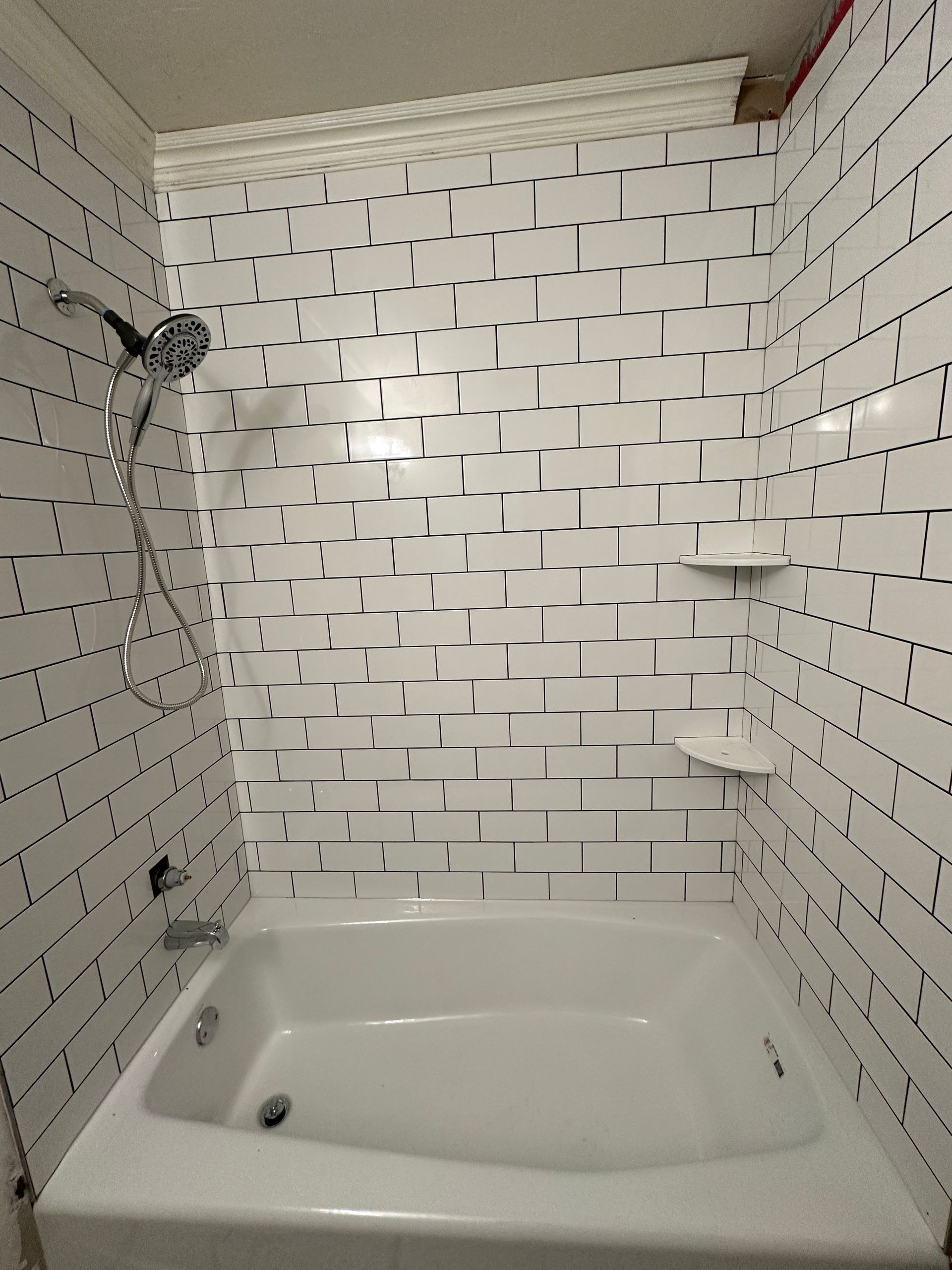 White-tiled bathroom with a bathtub, patterned wall tiles, and a shower head.
