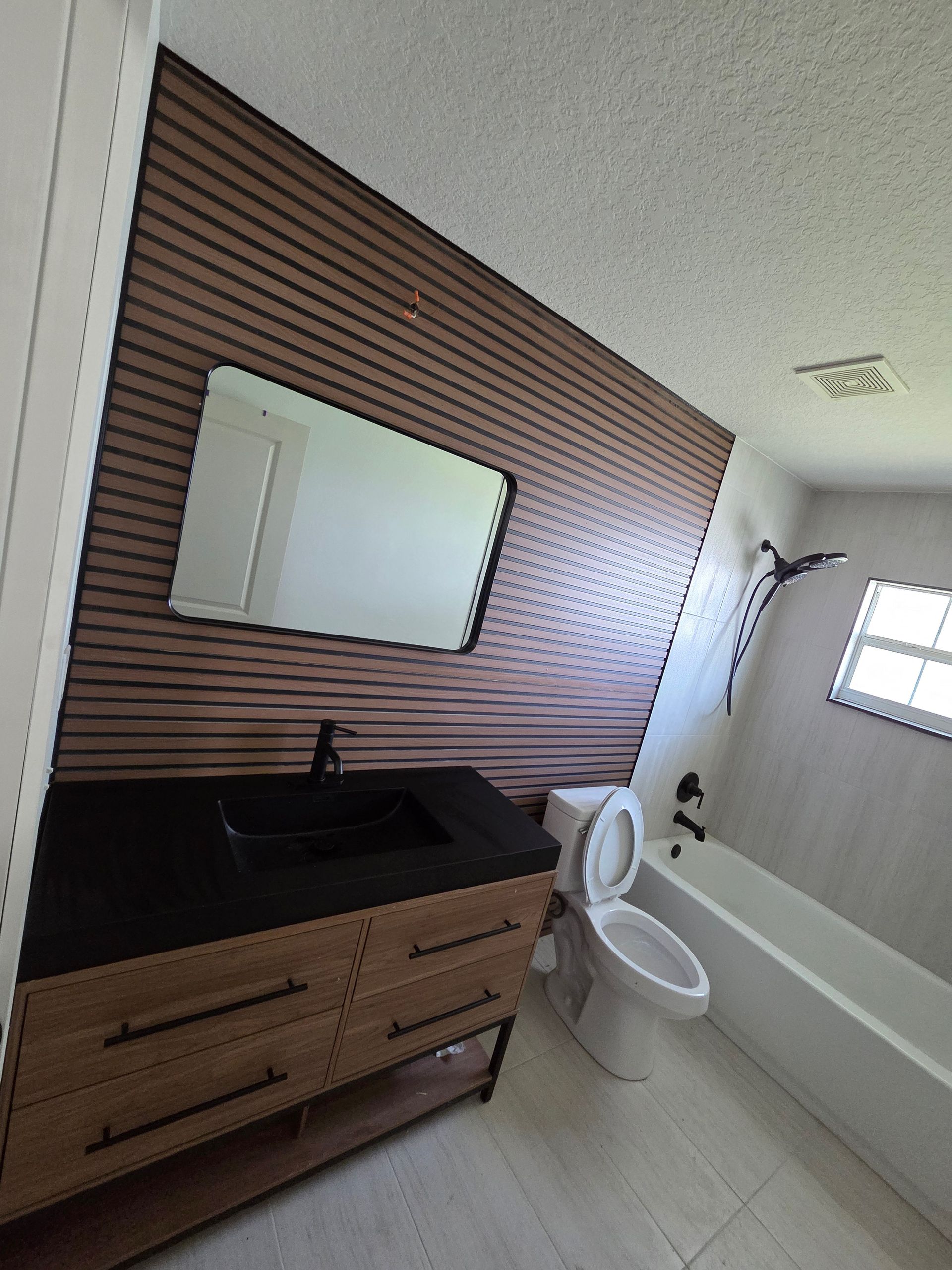 Bathroom with wood vanity, black sink, mirror, toilet, and bathtub beside a window.