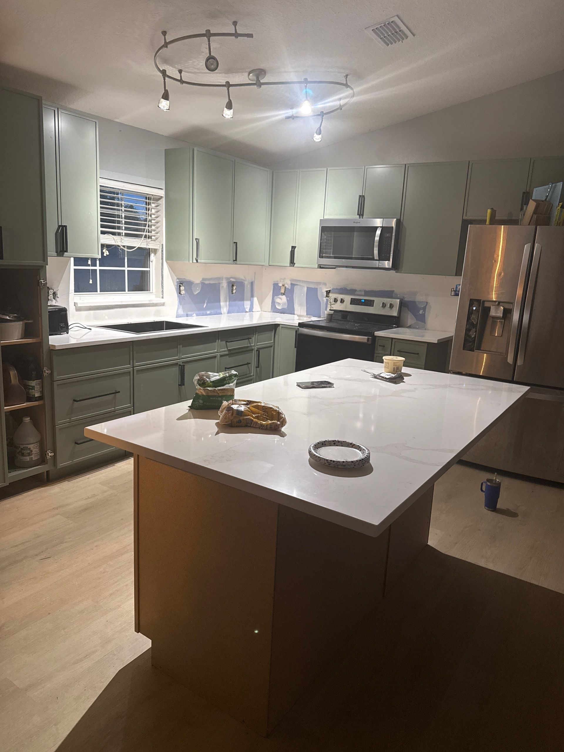 Modern kitchen with green cabinets, white island, and stainless steel appliances under ceiling lights