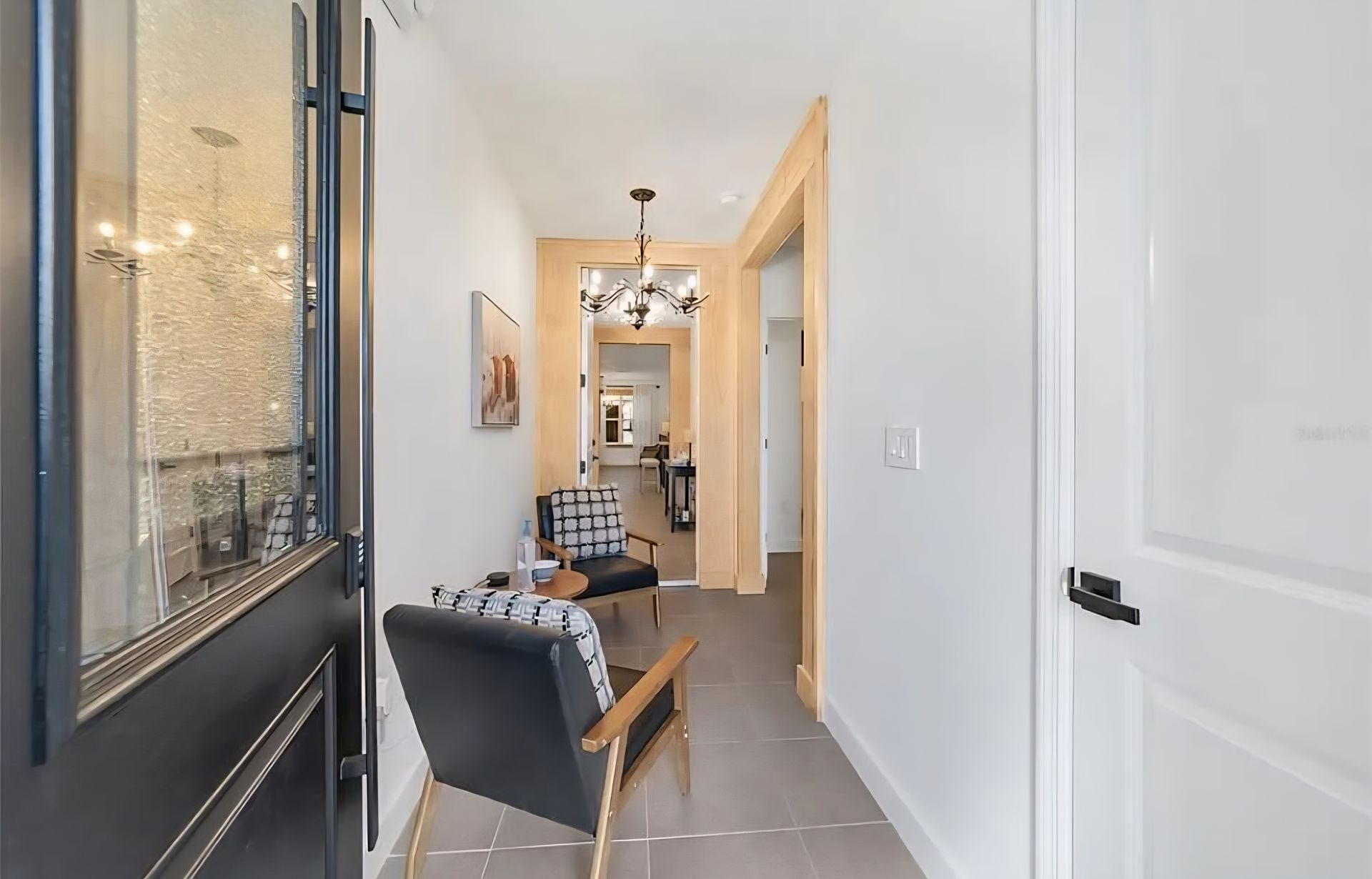 Bright hallway with black chairs, white walls, and a glass front door leading to a dining area