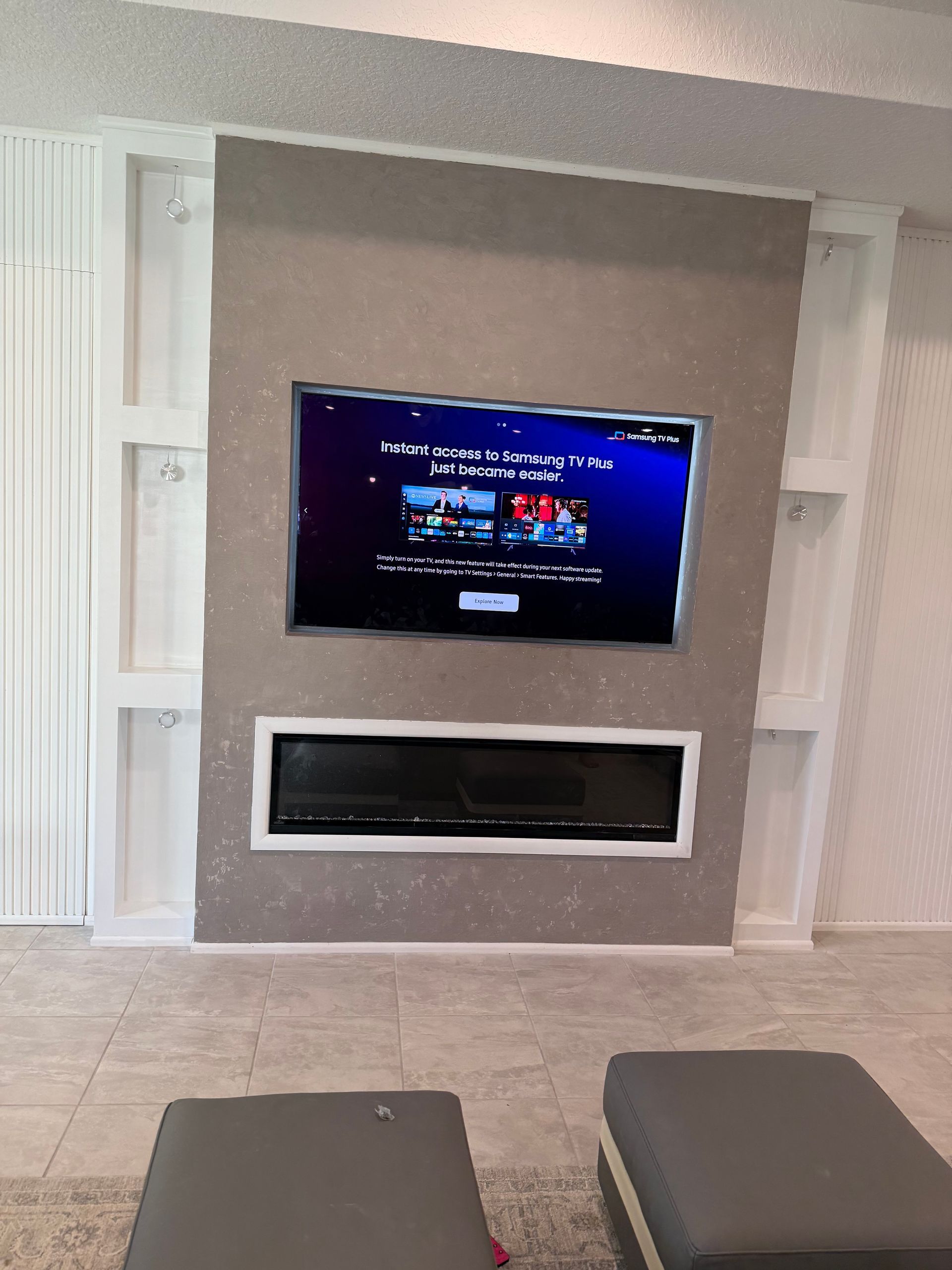 Modern living room wall with a mounted TV above a black fireplace, framed by white built-in shelves.