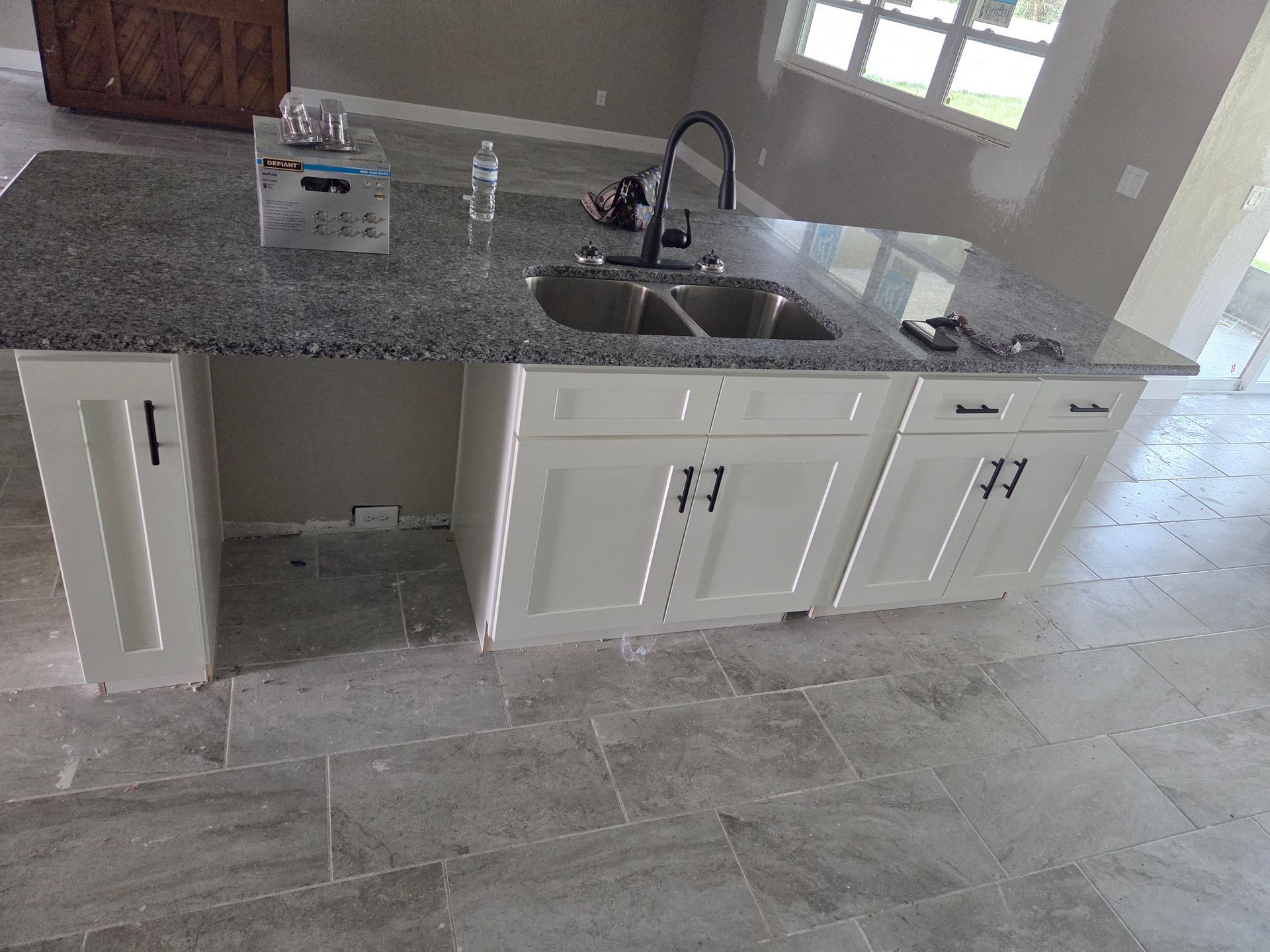 Kitchen with white cabinets, gray countertop, sink, and a tiled floor under a window.