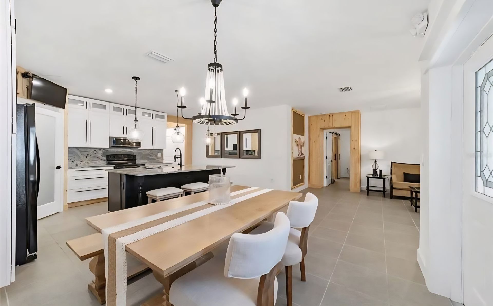 Bright modern kitchen and dining area with white cabinets, black island, and wooden table with chairs