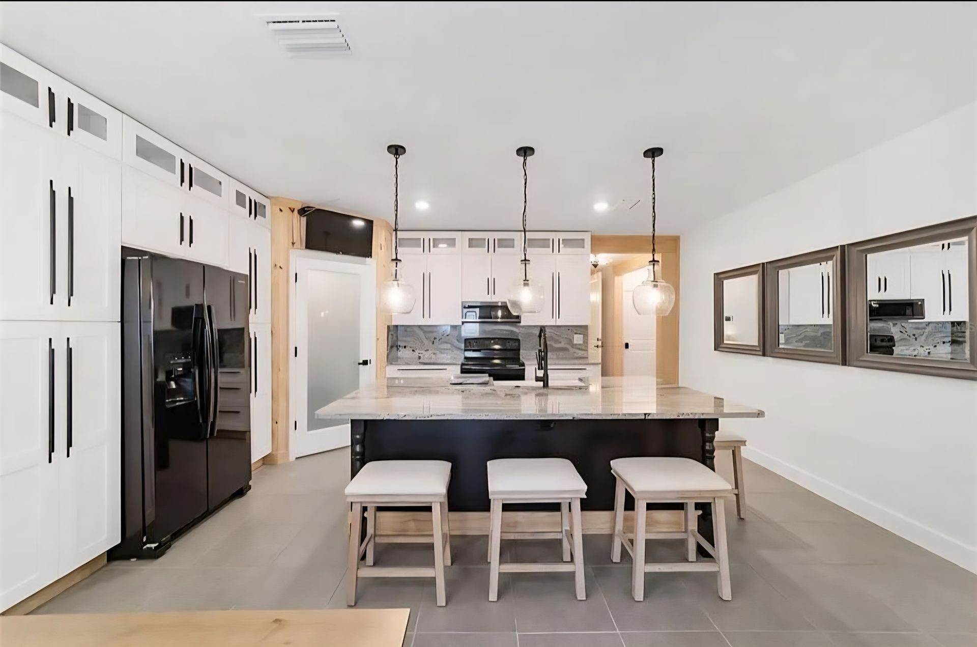 Modern kitchen with large island, black-and-white cabinets, pendant lights, and three stools