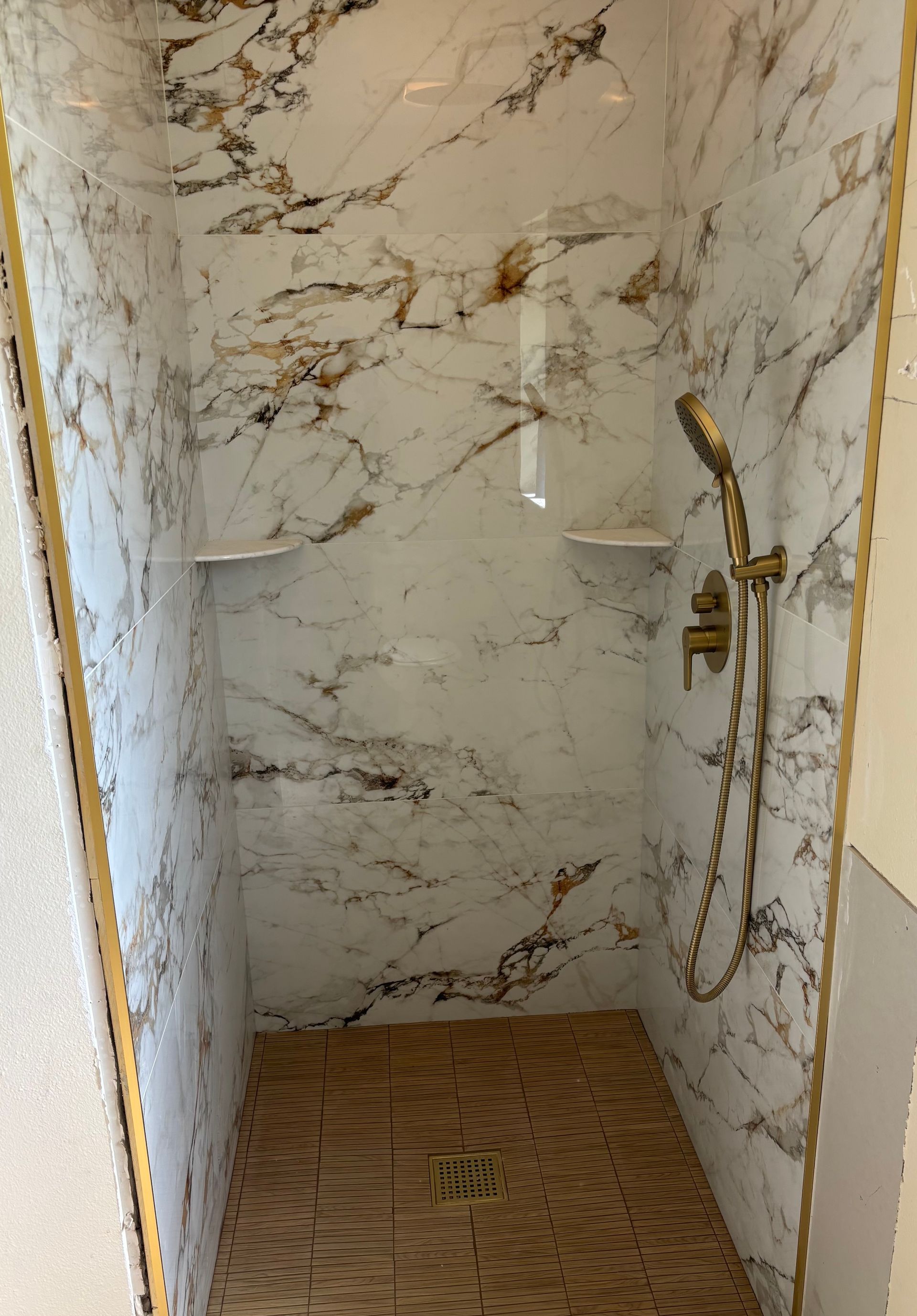Marble-tiled shower stall with a handheld showerhead and woven floor mat