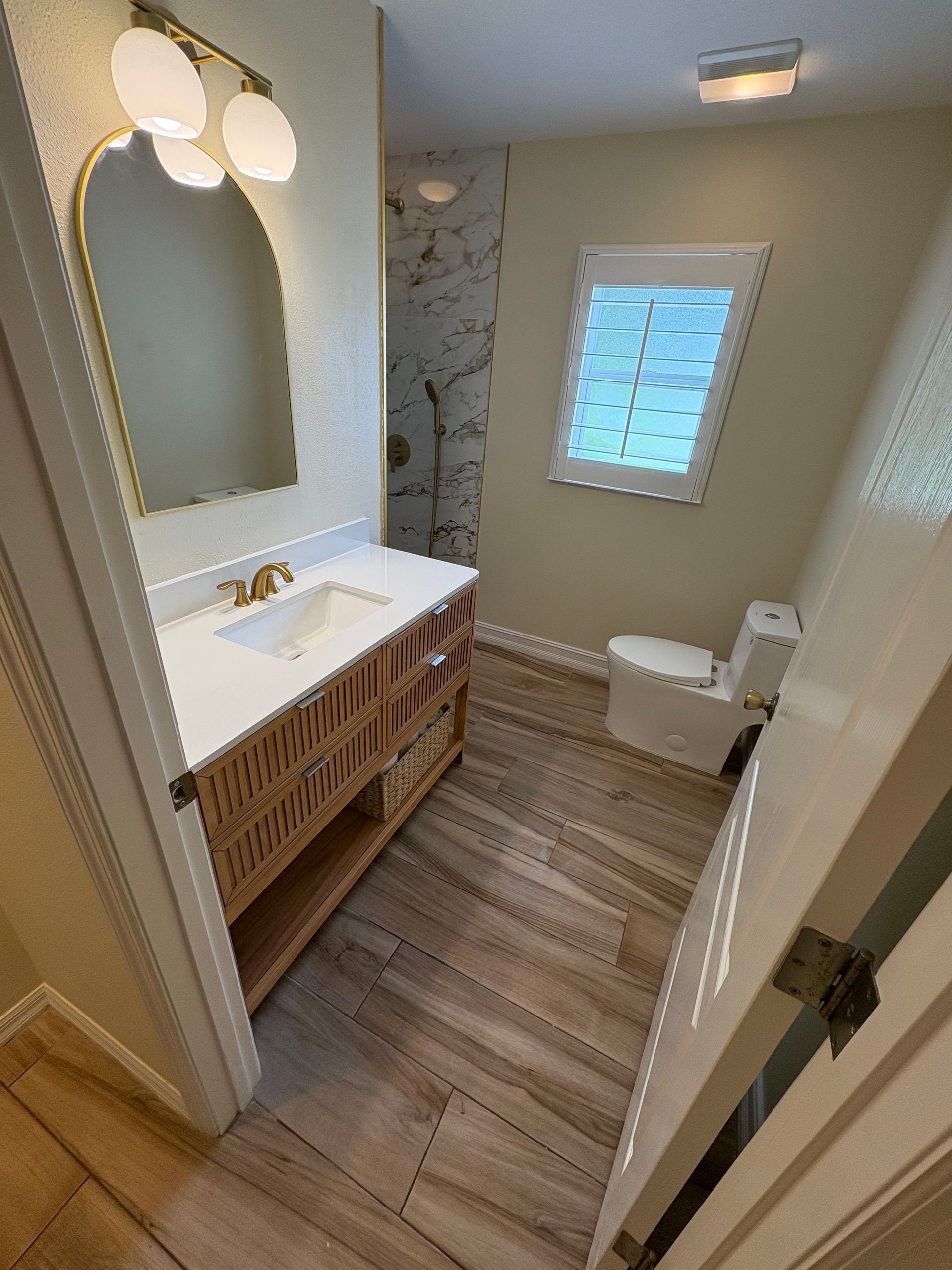 Small bathroom with white vanity, oval mirror, wood cabinet, window, and toilet.