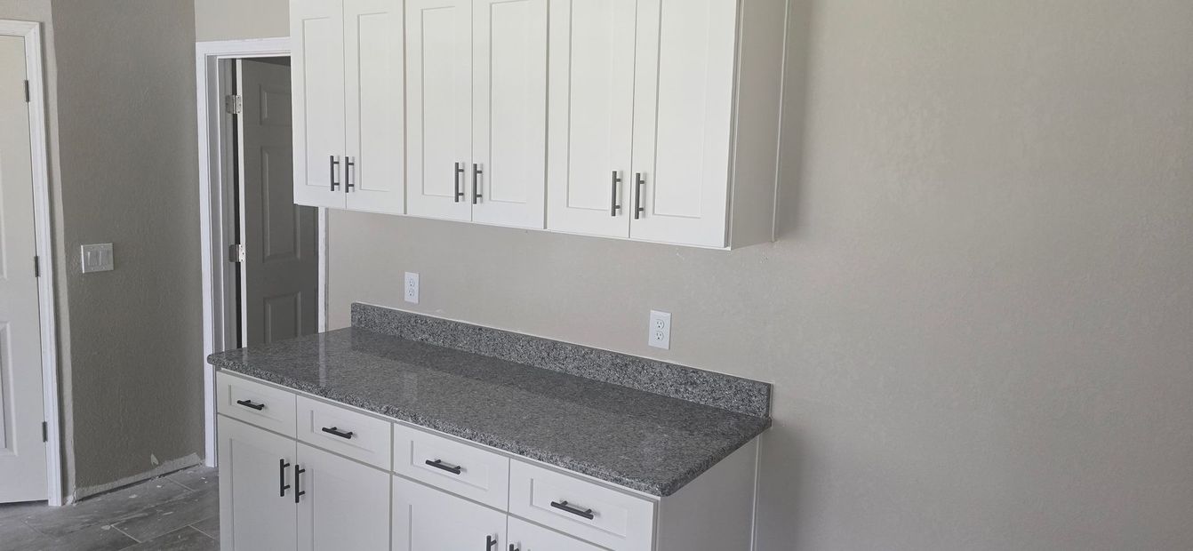 Kitchen with white cabinets, gray granite countertop, and stainless steel refrigerator.