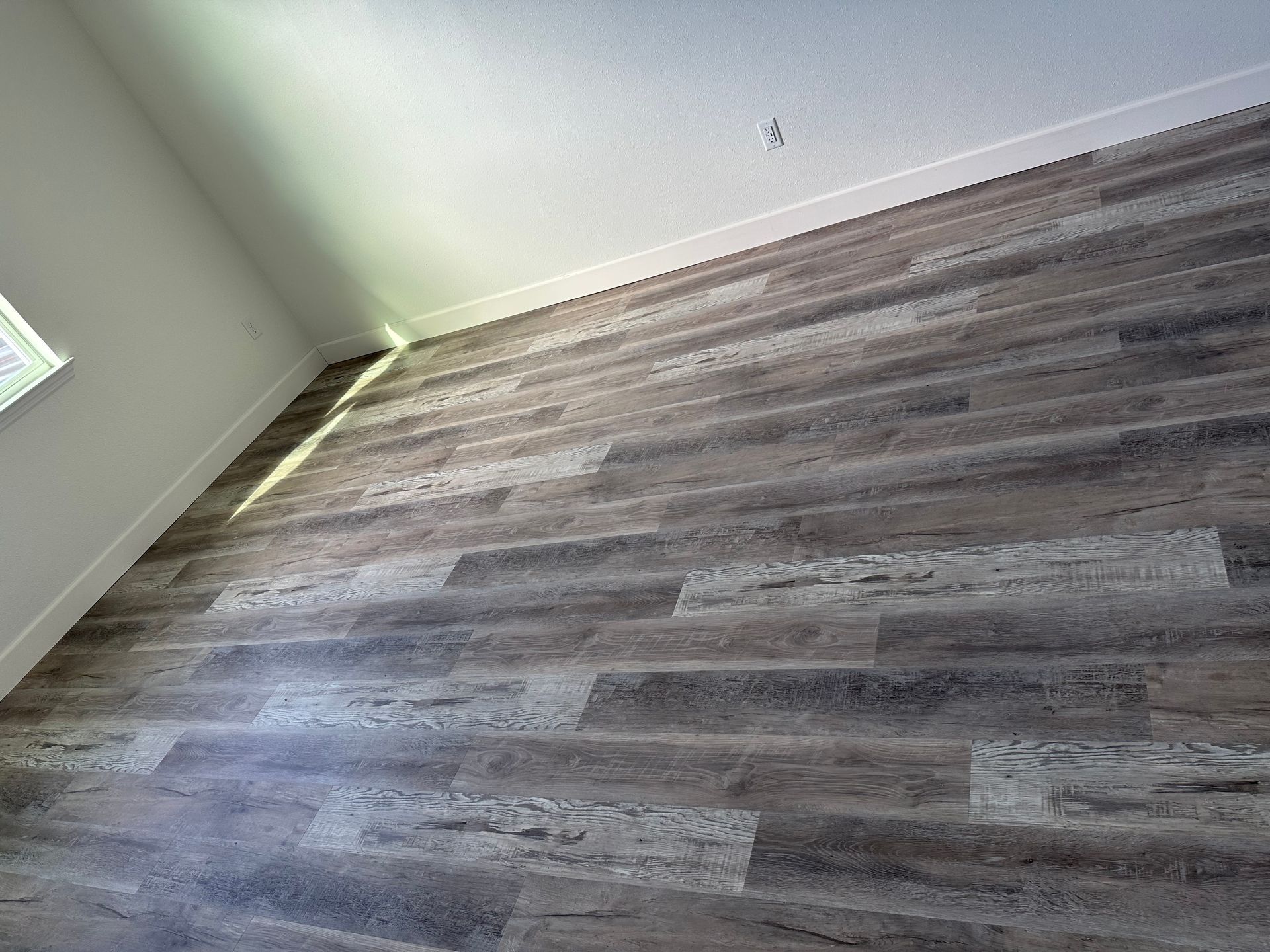 Empty room with gray wood-look flooring and white walls, seen at a slight angle.