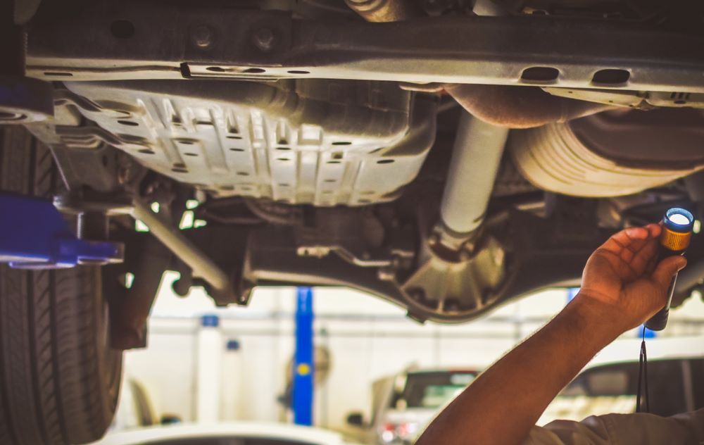 A Man is Looking Under a Car With a Flashlight — Sprint Mufflers, Exhausts & Mechanical Repairs in Stuart, NT