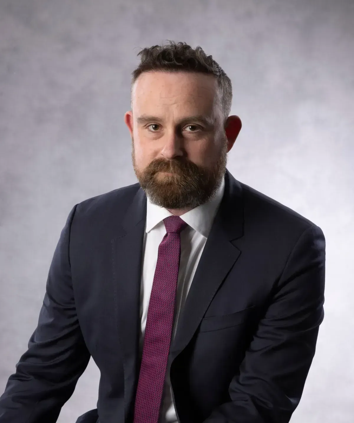 Studio portrait of a man in a dark suit, white shirt, and purple tie against a gray background