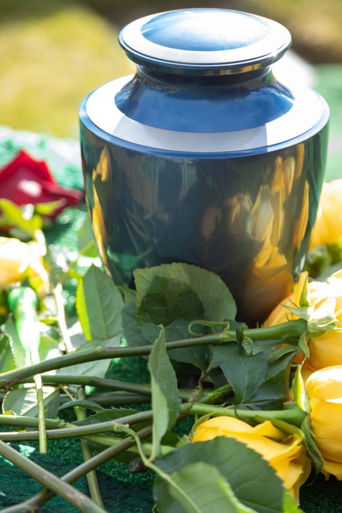 A Blue Urn Is Surrounded By Yellow Roses And Leaves On A Table — Territory Funerals In Palmerston, NT