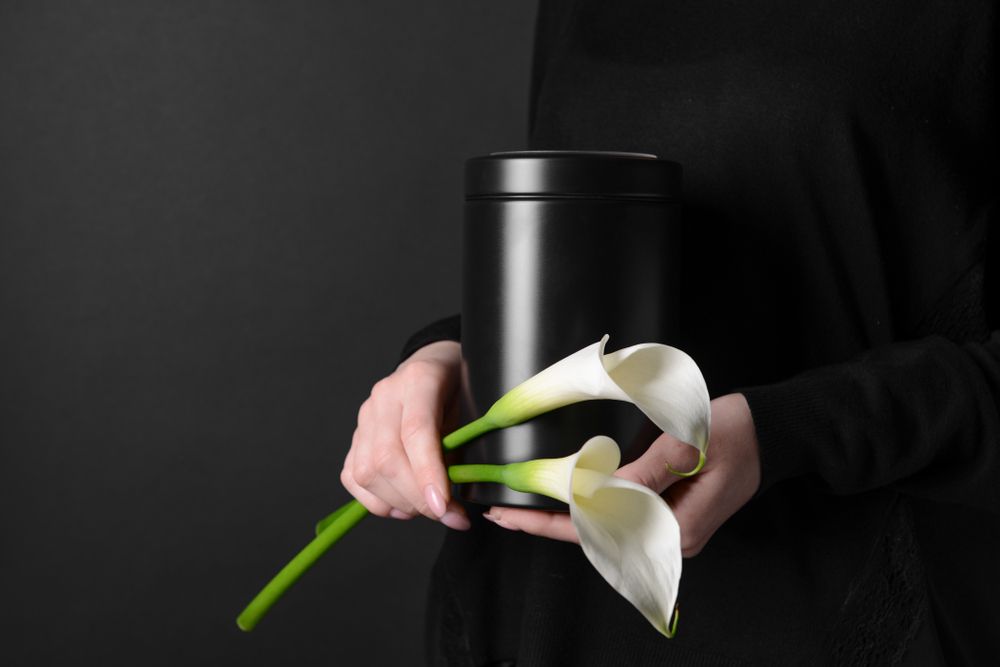 A Woman Is Holding A Black Urn With White Flowers In Her Hands — Territory Funerals In Leanyer, NT