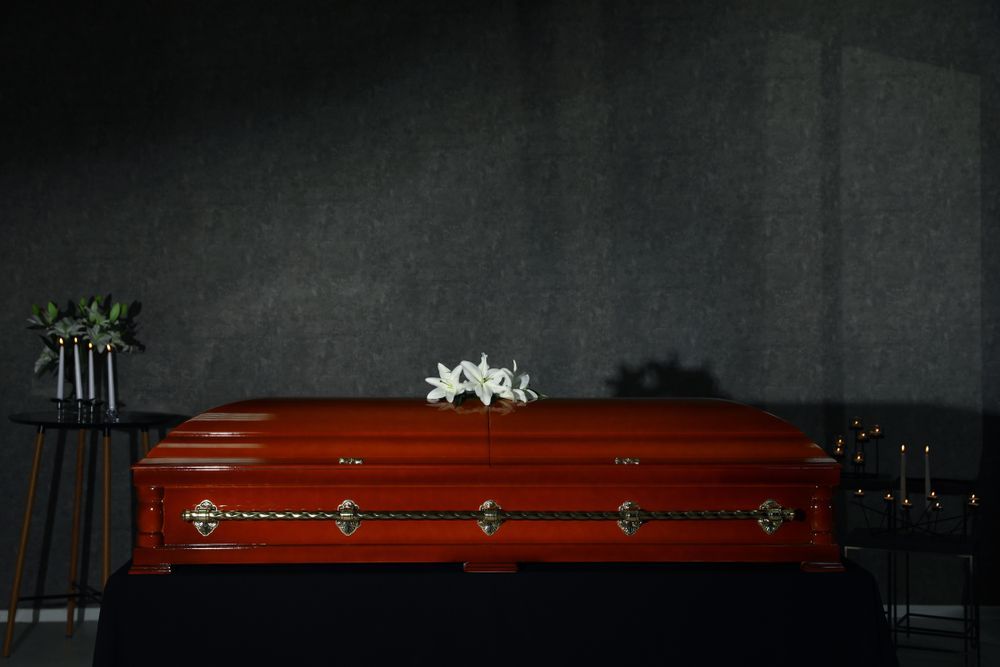 A Wooden Coffin With Flowers On Top Of It In A Dark Room — Territory Funerals In Yarrawonga, NT