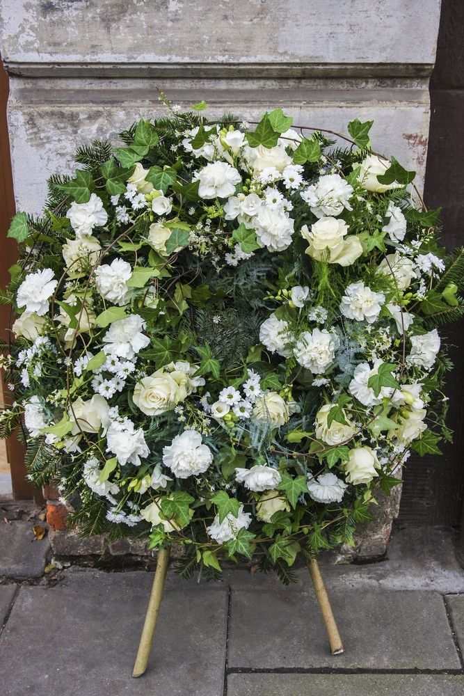 A Wreath Of White Flowers Is Sitting On A Tripod On The Sidewalk — Territory Funerals In Yarrawonga, NT