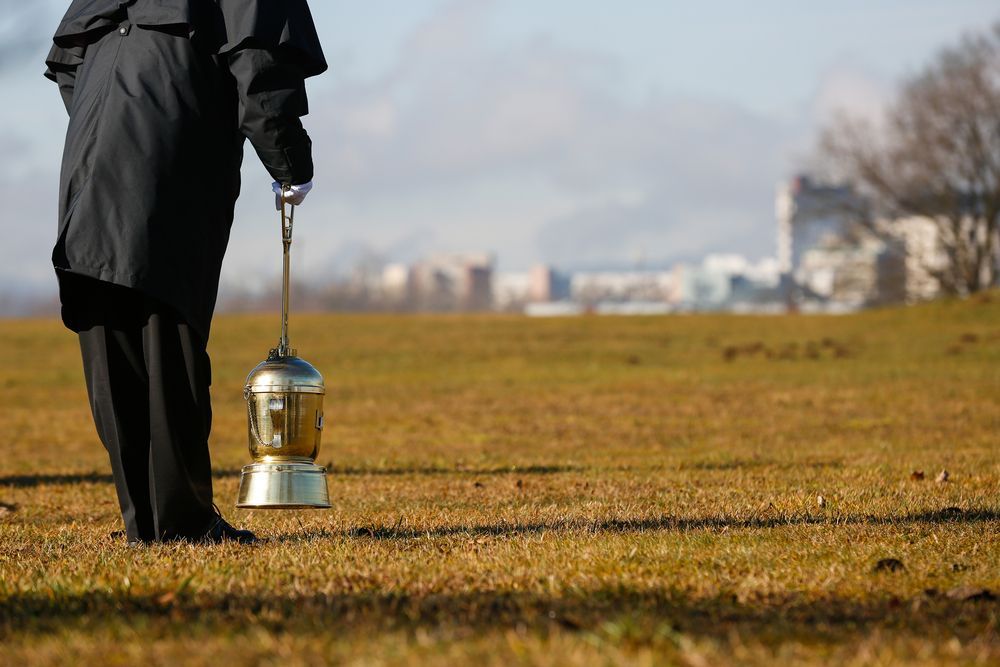 A Man Is Holding A Urn In A Field — Territory Funerals In Zuccoli, NT