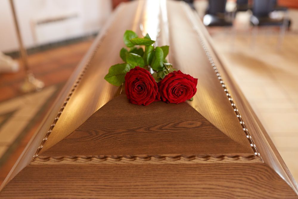 A Wooden Coffin With Two Red Roses On Top Of It — Territory Funerals In Yarrawonga, NT
