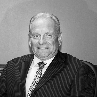 A headshot of a person in a pinstriped suit and patterned tie smiling against a plain backdrop in black and white.