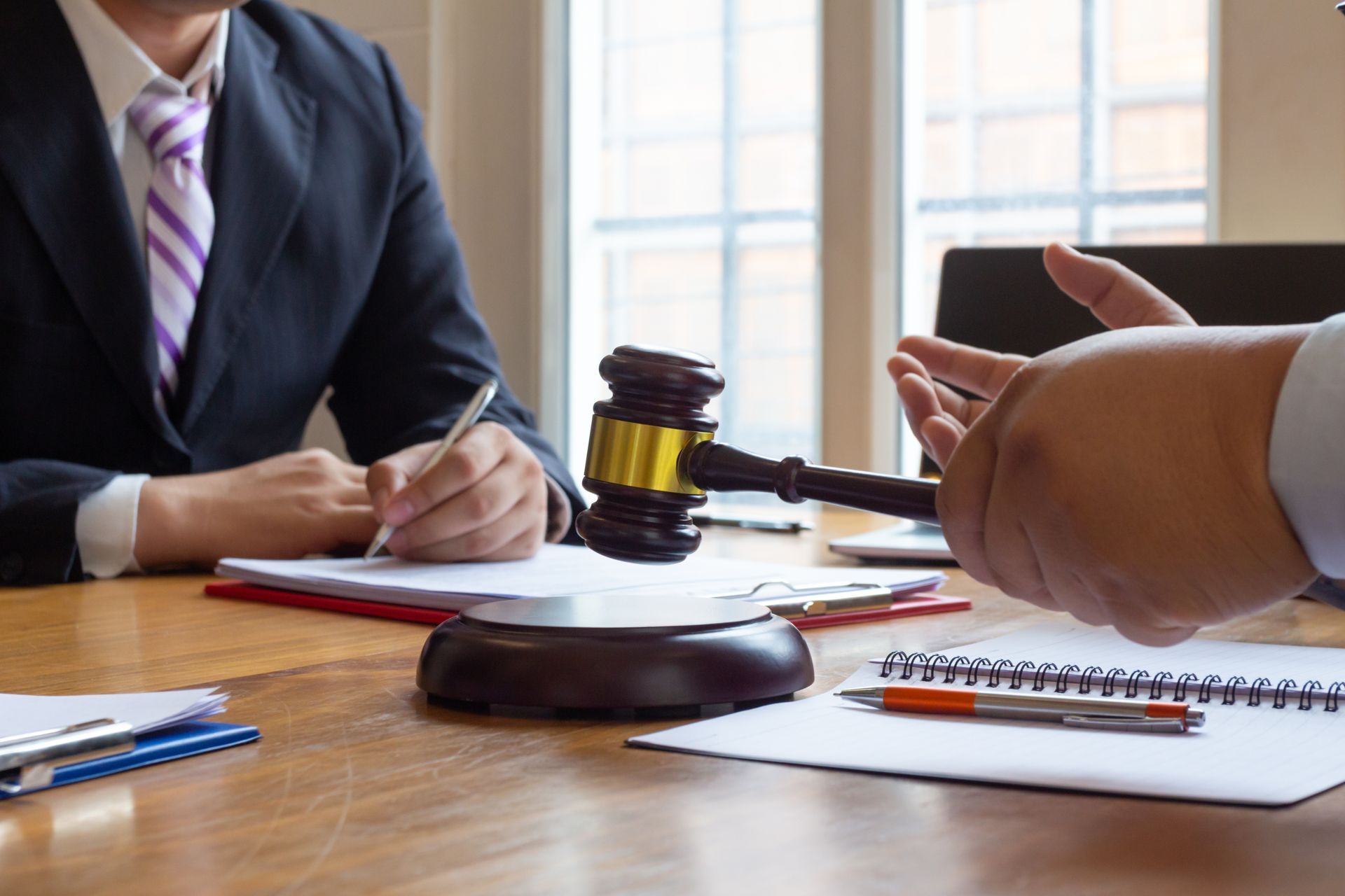 A judge’s gavel rests on a wooden table between two people in business attire engaged in a discussion.