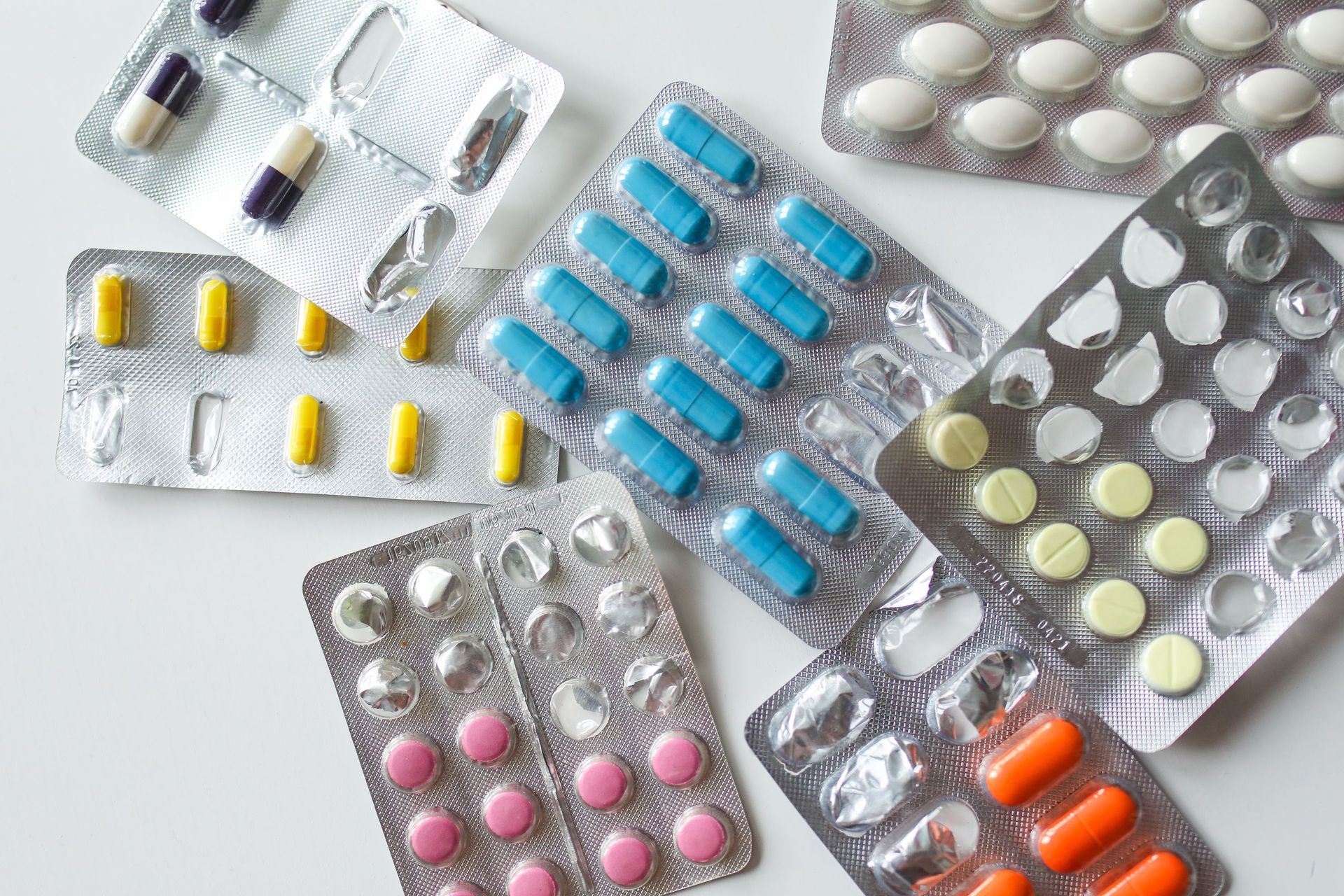 Assorted blister packs of colorful pills and capsules on a white surface