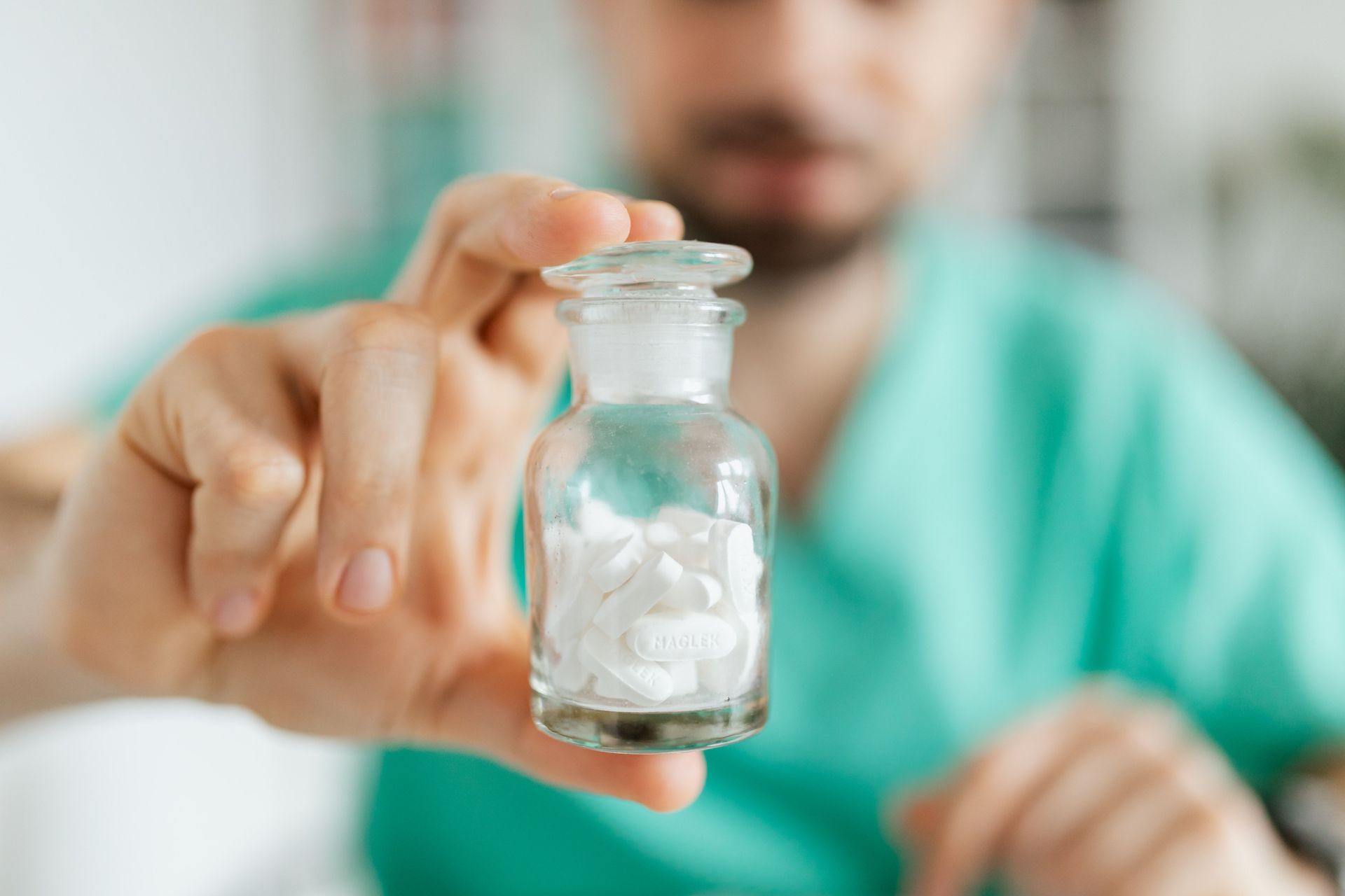Person in green scrubs holding a small glass vial with clear liquid in a lab setting