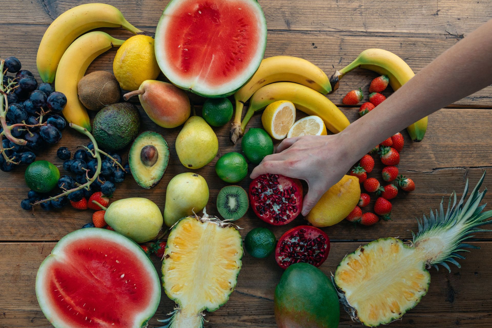 Assorted colorful tropical fruits on a wooden table, with a hand reaching for dragon fruit