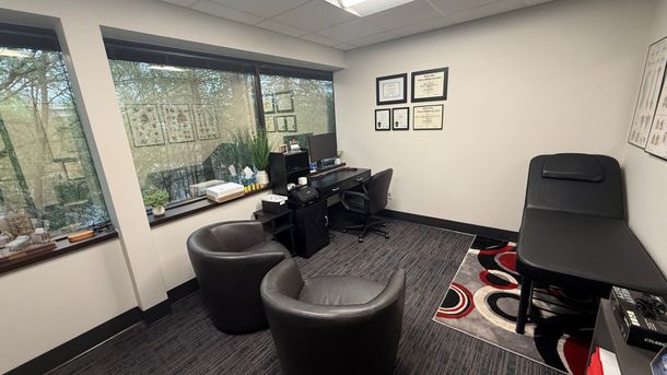 Small office with black chairs, desk, computer, large windows, and patterned rug.