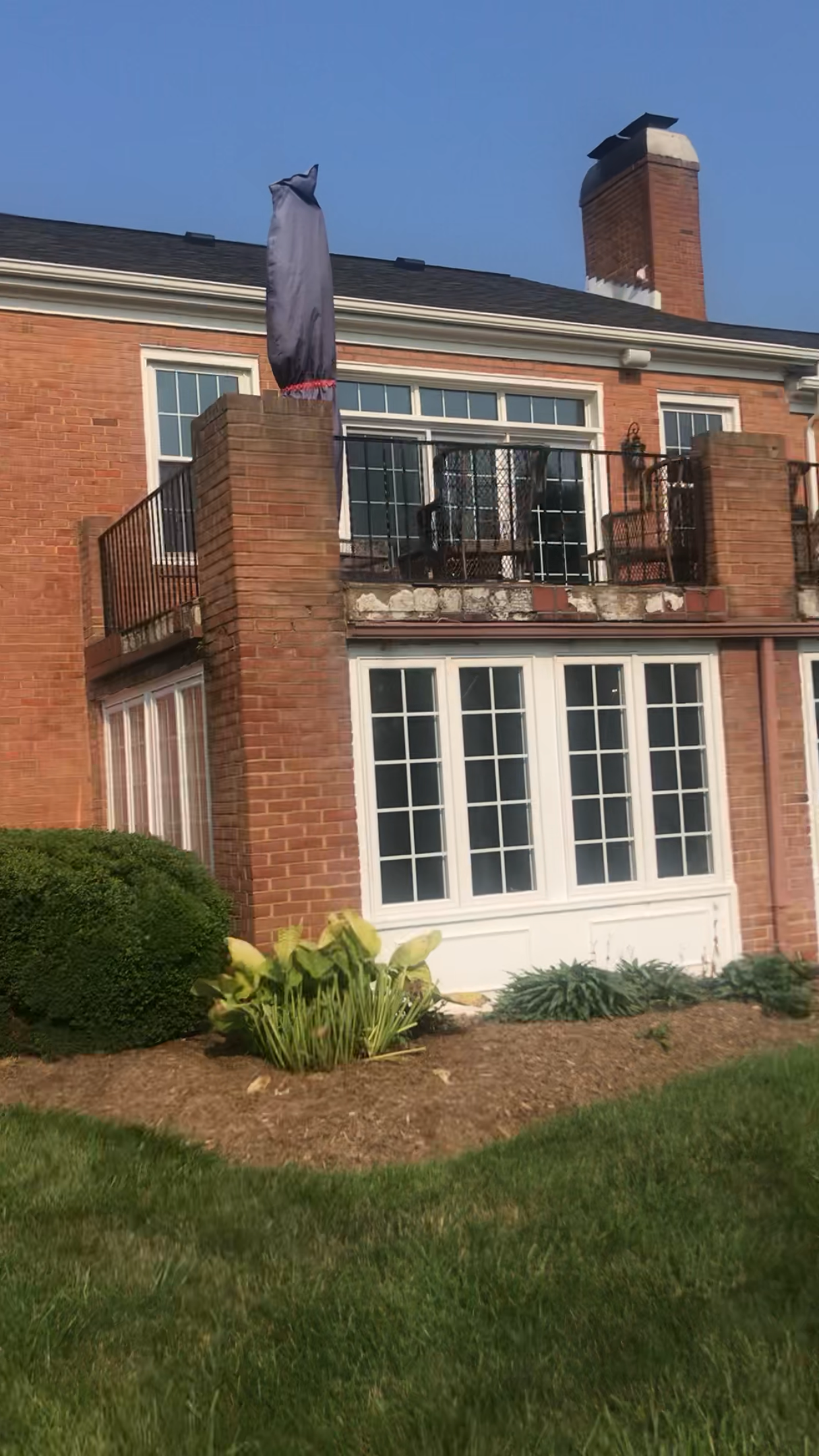Brick building with second-story balcony and chimney. A bush and lawn are in the foreground. Blue sky.