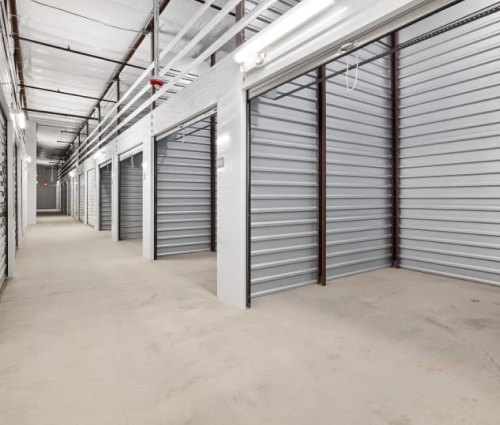 Empty indoor storage unit hallway with gray roll-up doors and concrete floor