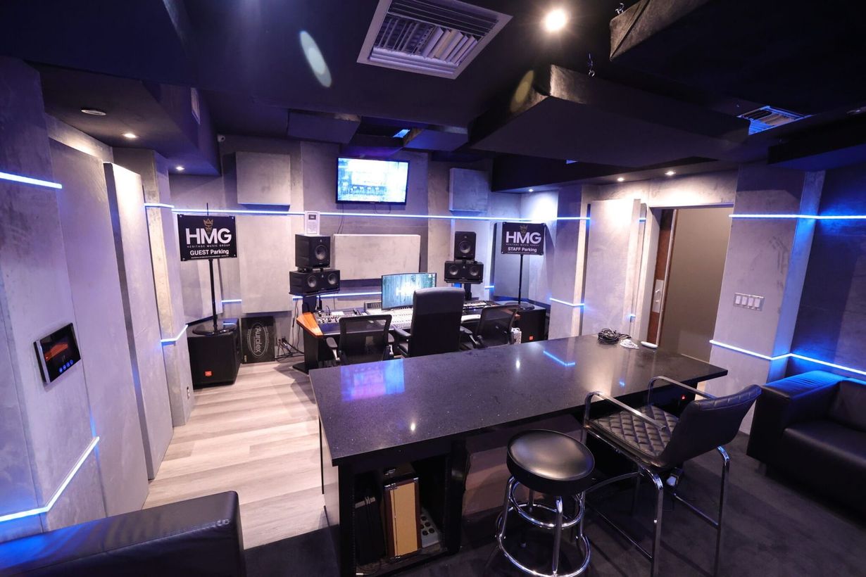 Modern lounge with tables, stools, and wall-mounted monitors in a dimly lit room with blue accent lighting.