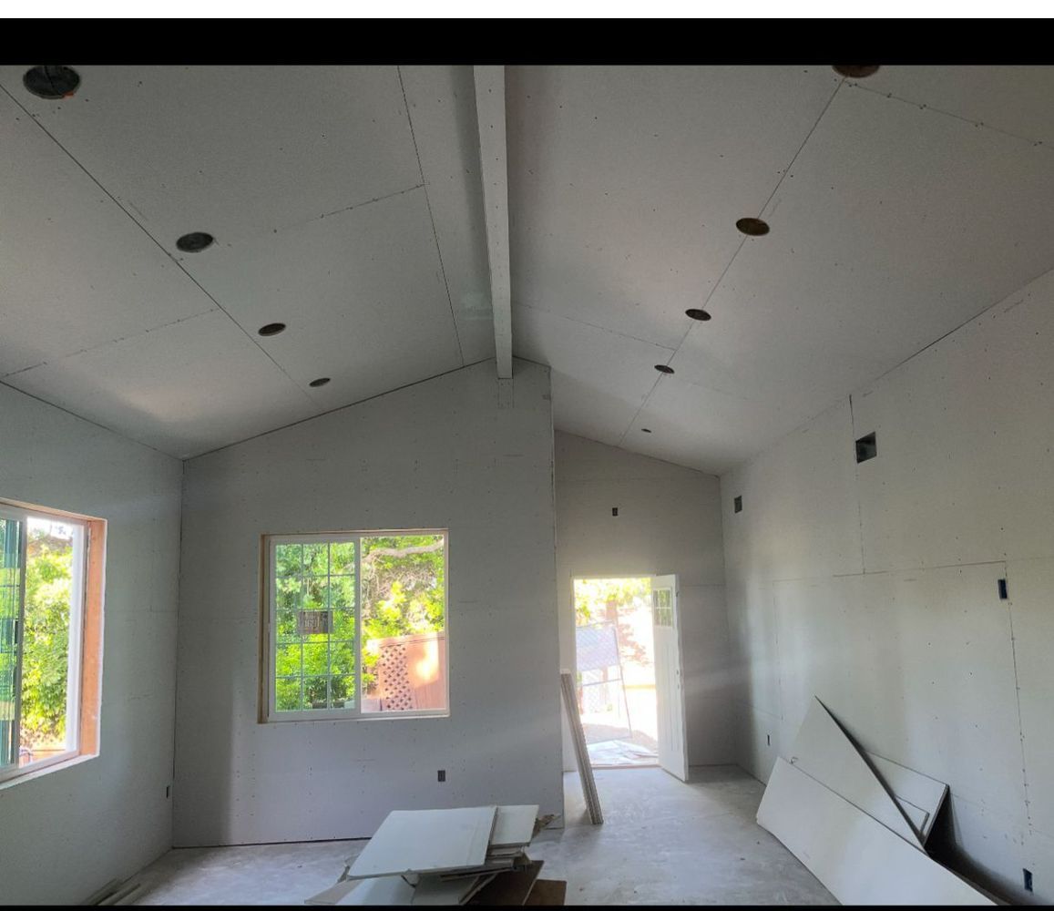 Interior of a room under construction with drywall on walls and ceiling, windows, and recessed lighting.
