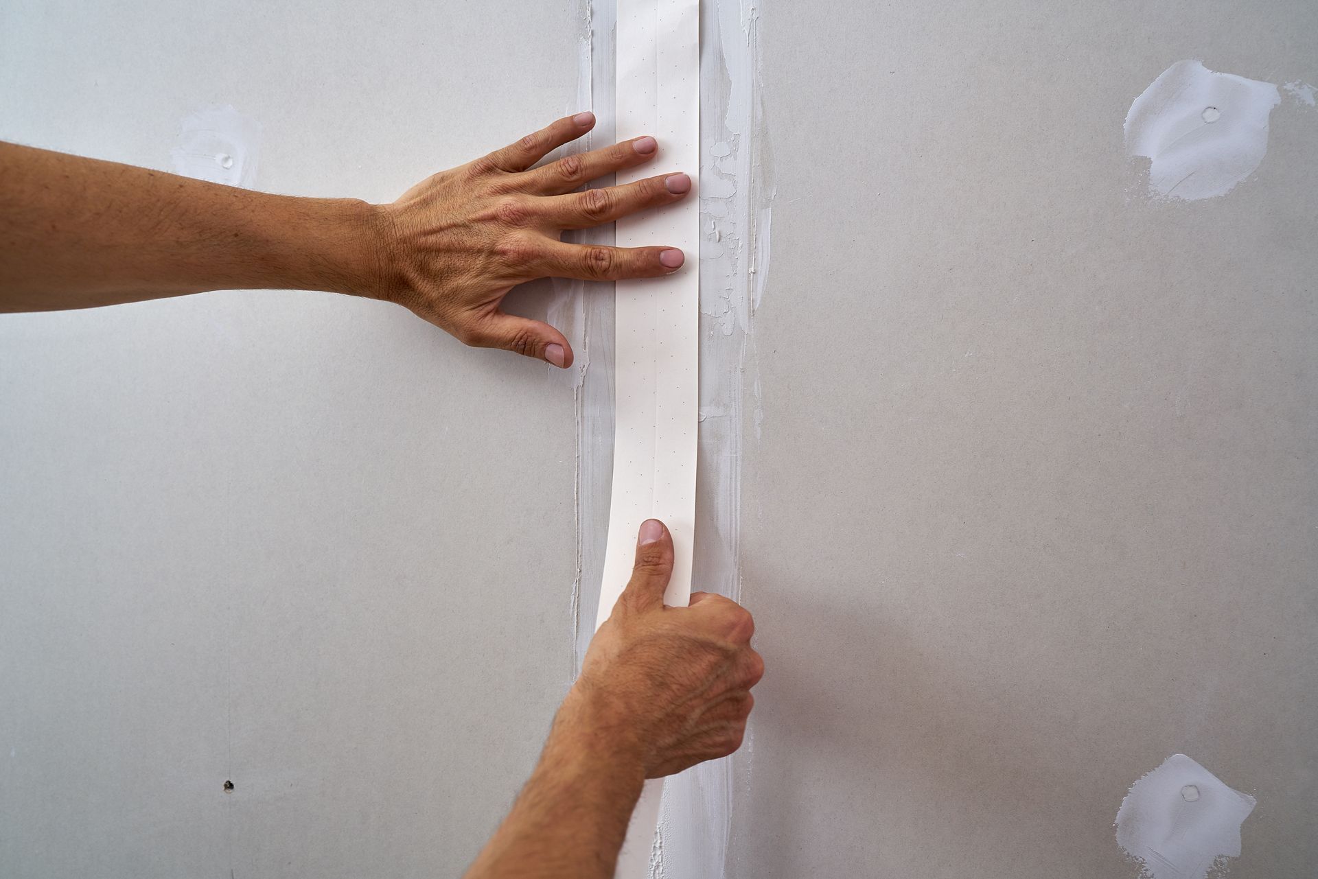 Hands applying joint tape to a drywall seam.