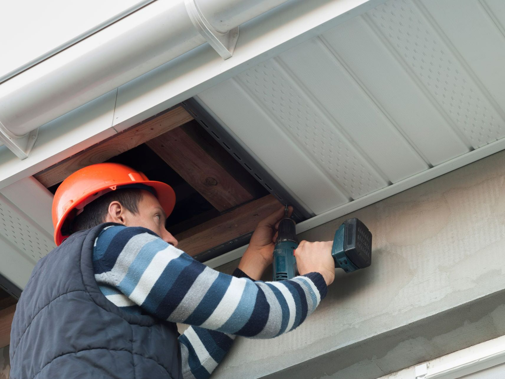 A man wearing a hard hat is working on the ceiling of a building.