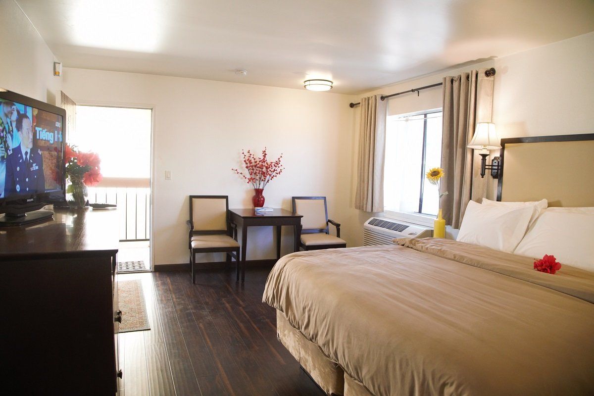 Hotel room with a bed, chairs, TV, and doorway to a balcony.