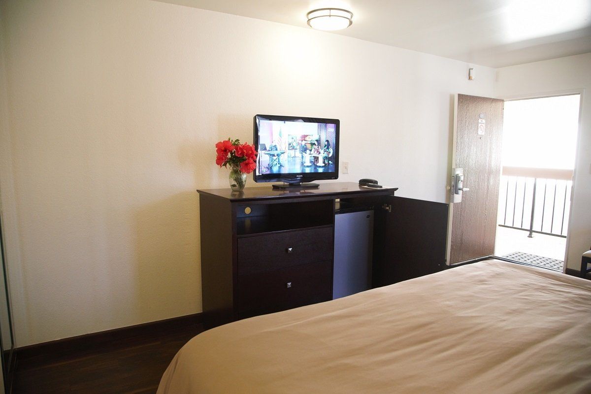 Bedroom with TV on a dark brown dresser, open door to a balcony.