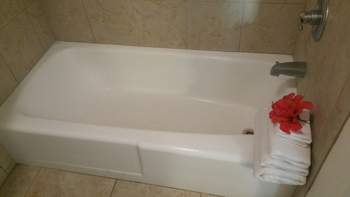 White bathtub with stacked white towels and red flowers in a bathroom with beige tile.