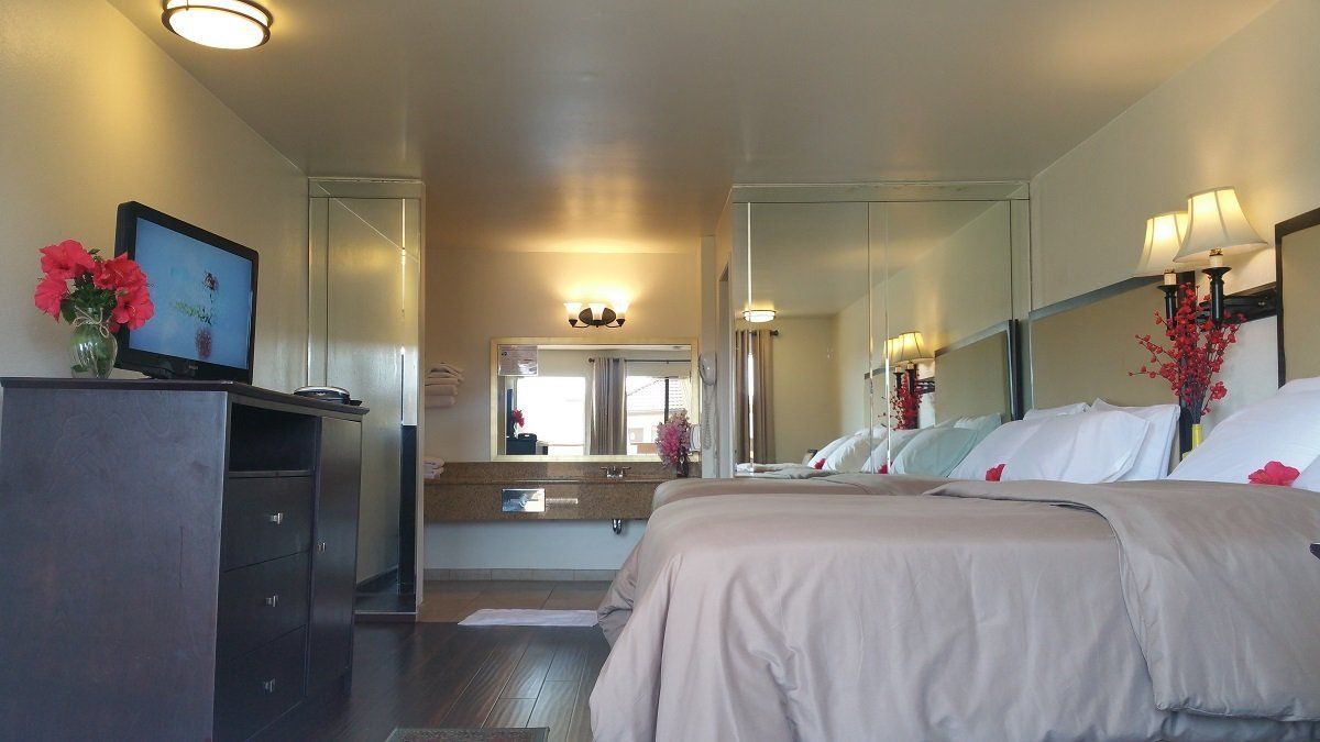Hotel room with two beds, TV, and mirrored wall.