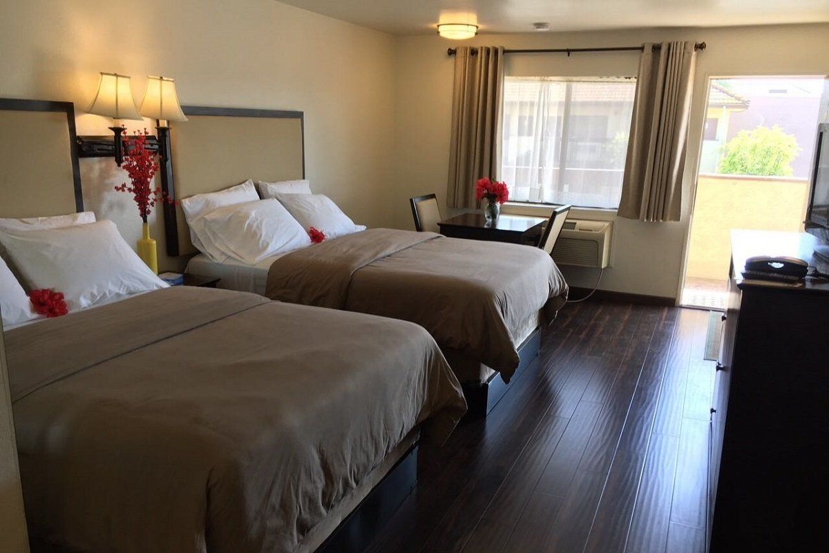 Two beds in a motel room. Brown bedding, wood floors, small table.