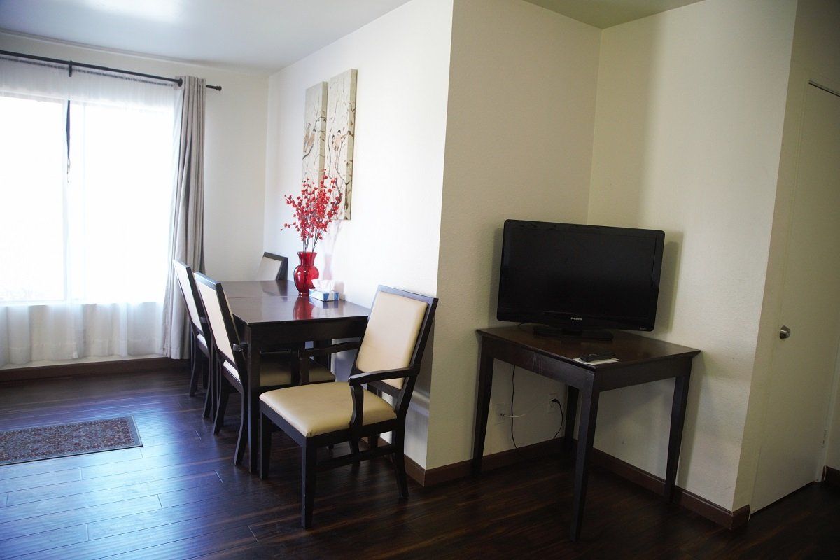 Dining room with dark wood table and chairs, TV on a stand, and window with curtains.