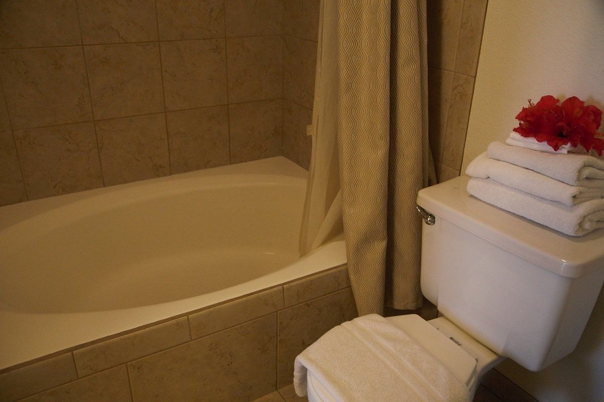 Bathroom with a white bathtub, toilet, and stacked white towels with red flowers. Tan tile.