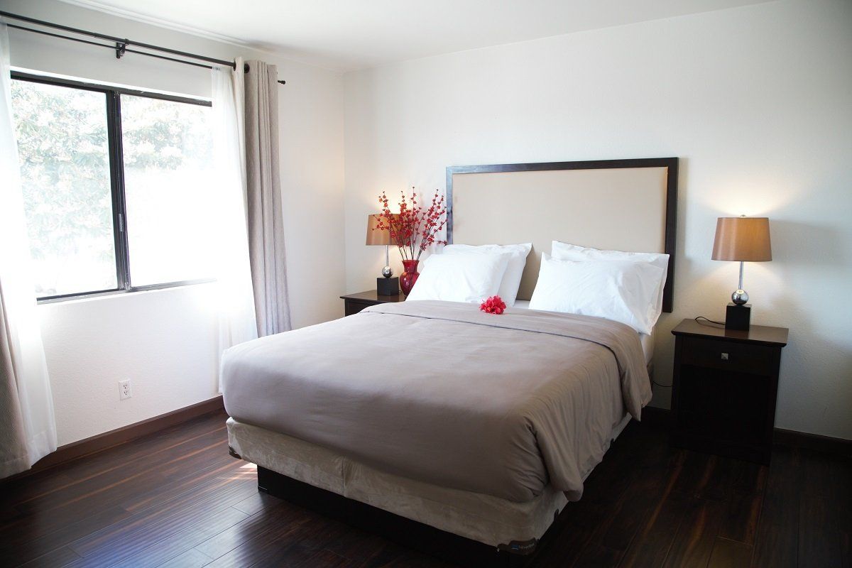 Bedroom with a queen bed, nightstands, window, and dark wood floor. Beige, white and dark brown color scheme.
